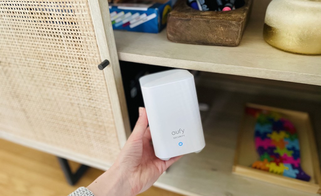 hand holding a white eufy home base in front of caned cabinet