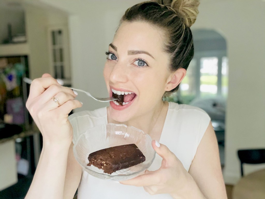 woman holding plate with protein bar taking bite off fork