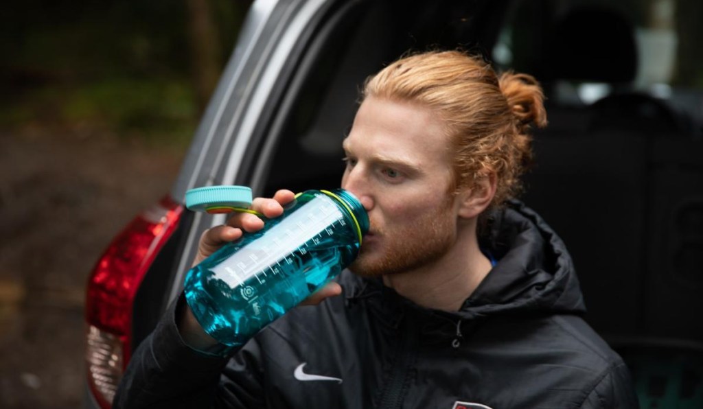 man drinking from blue water bottle on tailgate of vehicle