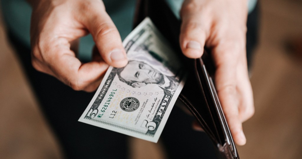 person putting a 5 dollar bill into a wallet