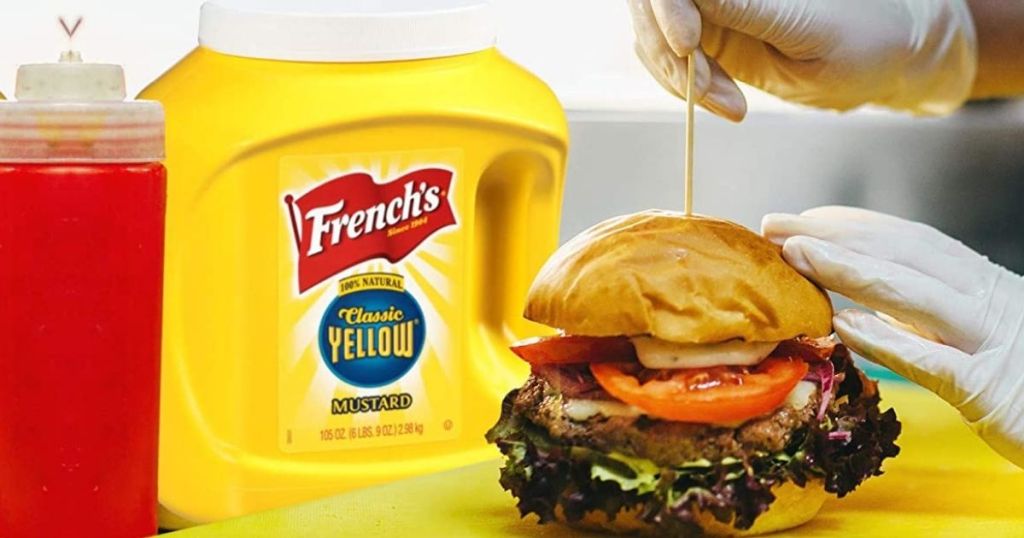 Huge tub of French's Yellow Mustard next to a burger