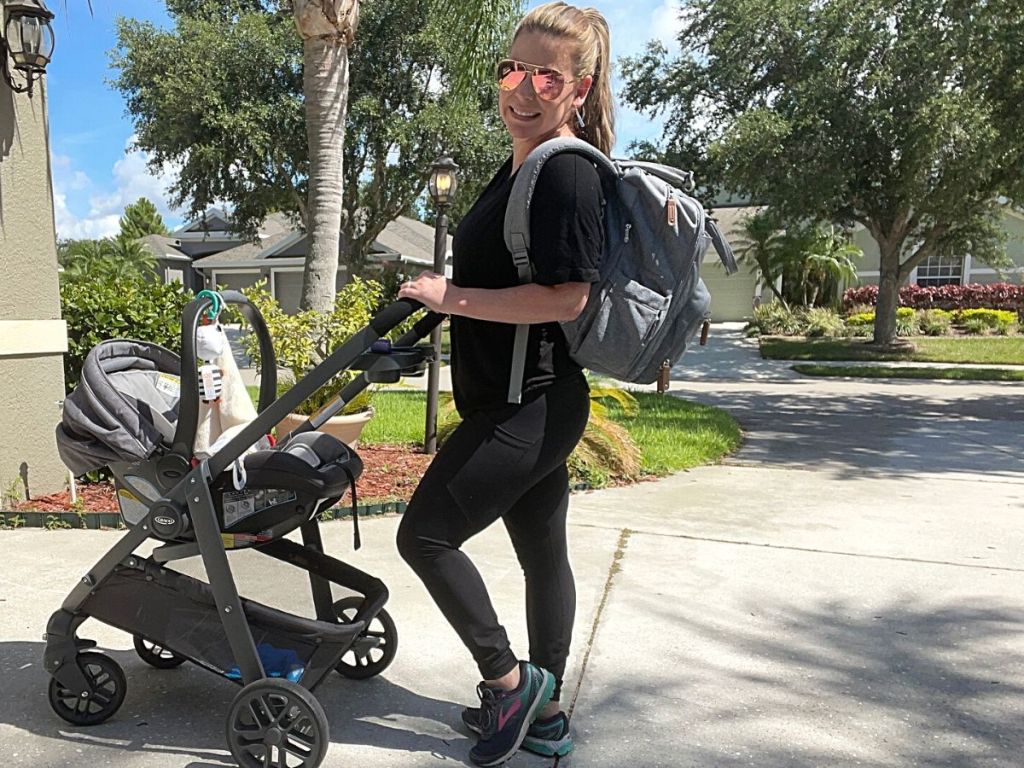 woman wearing sunglasses and gray diaper bag backpack pushing stroller