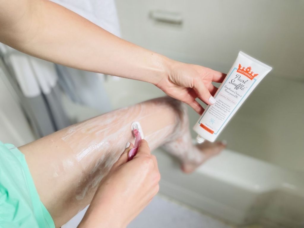 woman shaving her legs with one hand and holding Shaveworks shaving cream with the other