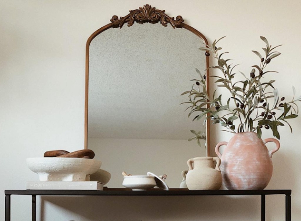 gold antique mirror sitting on black entryway table with various pottery decor