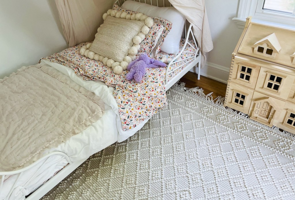 corner of kids bedroom with boho knotted rug and bed with flowers and pillow