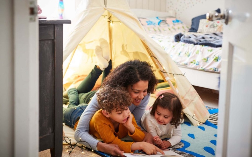 mother reading to two children on bedroom floor