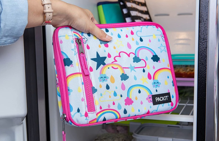 hand holding a rainbow lunchbox in front of open refrigerator