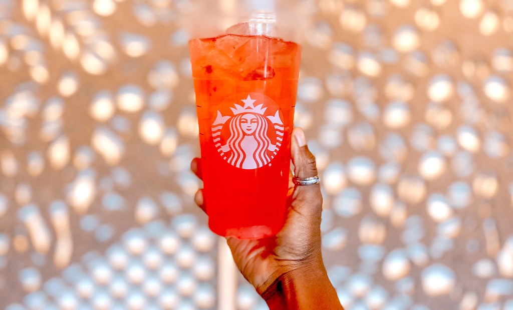 hand holding up a red colored starbucks iced gummy bear drink with lights on wall in background