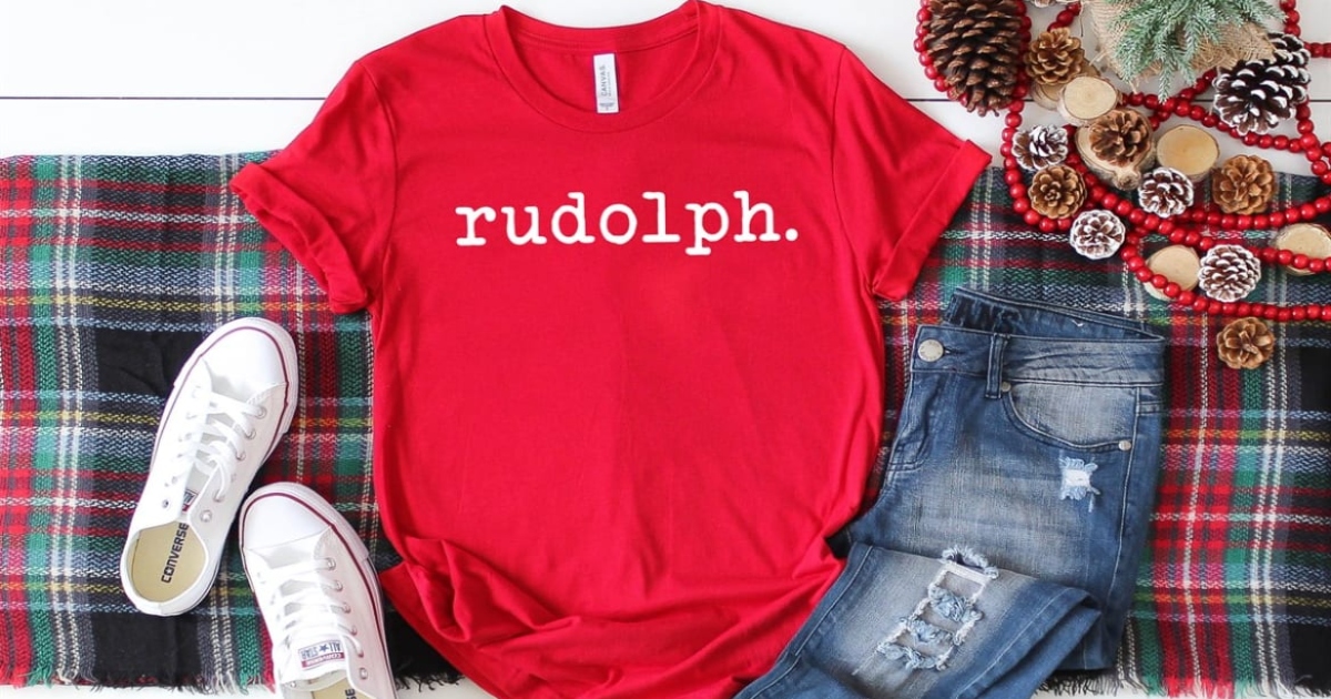 red rudolph tee laying out with a pair of jeans and white sneakers on a plaid holiday table runner