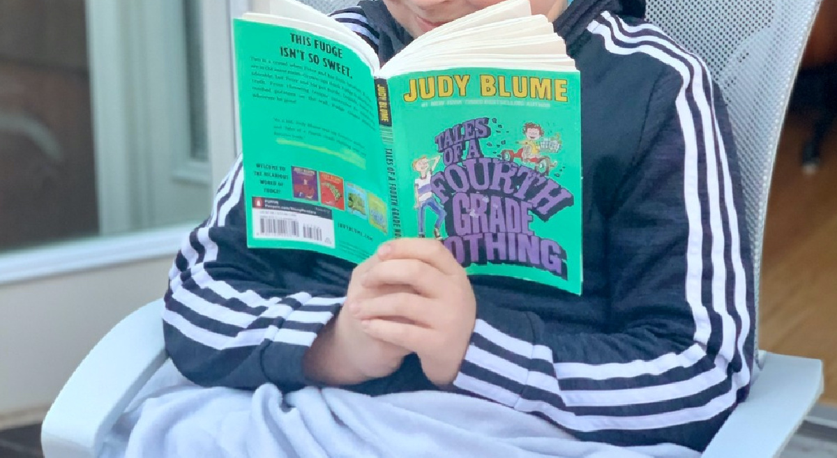 boy reading book sitting on patio chair