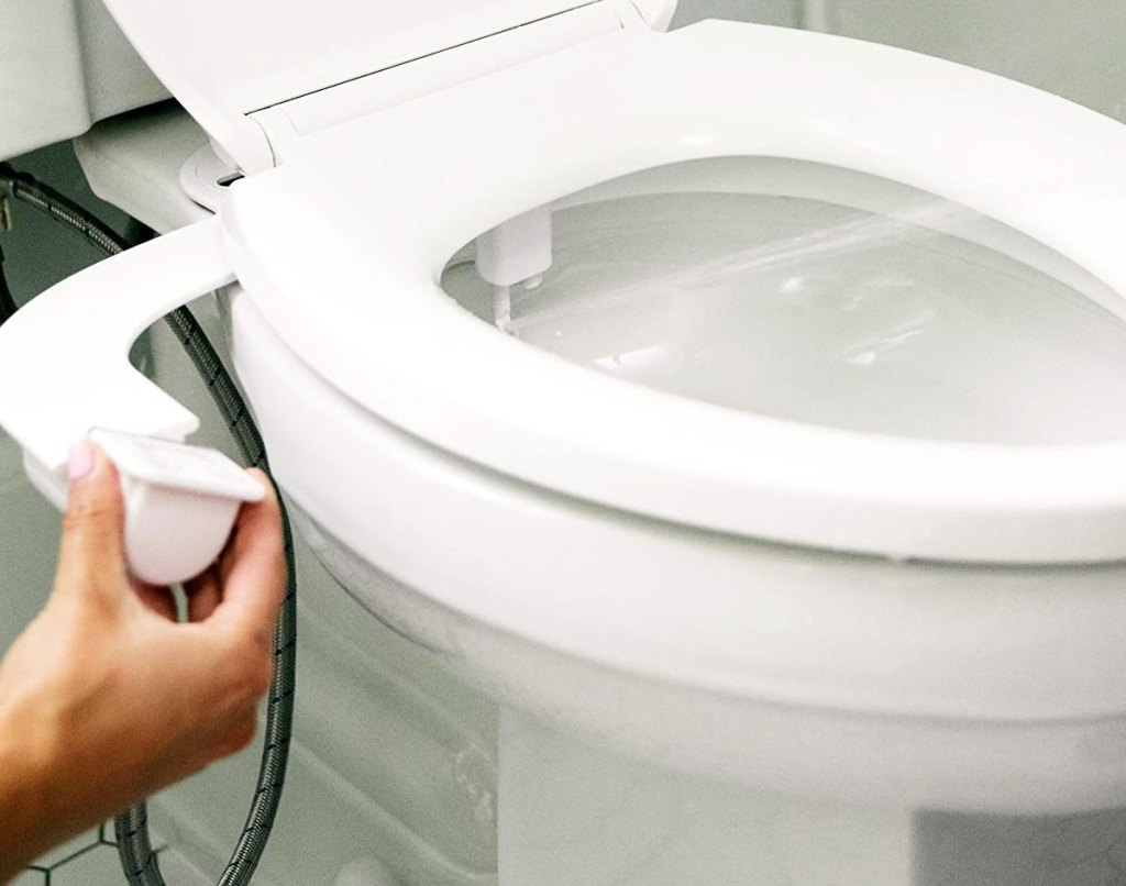 hand adjusting bidet attachment on toilet