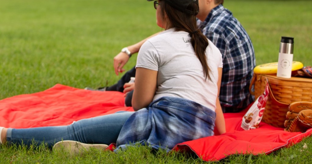 2 people sitting on red puffy camping blanket 