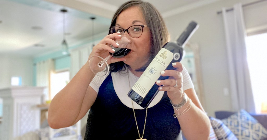 woman drinking red wine from glass while holding up bottle