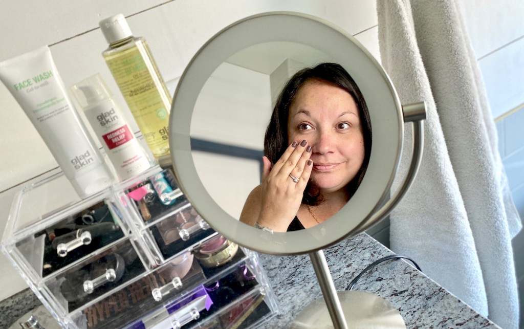 woman with hand on face looking in bathroom mirror