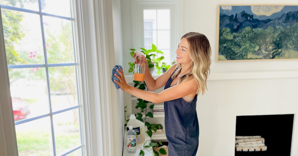 woman wiping down wall with microfiber cloth and spray bottle in living room