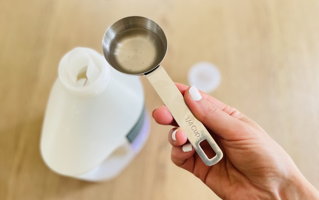 hand holding measuring cup of with clear laundry detergent inside for how to clean walls