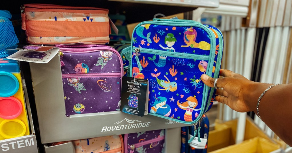 hand holding blue lunchbox with mermaids on it