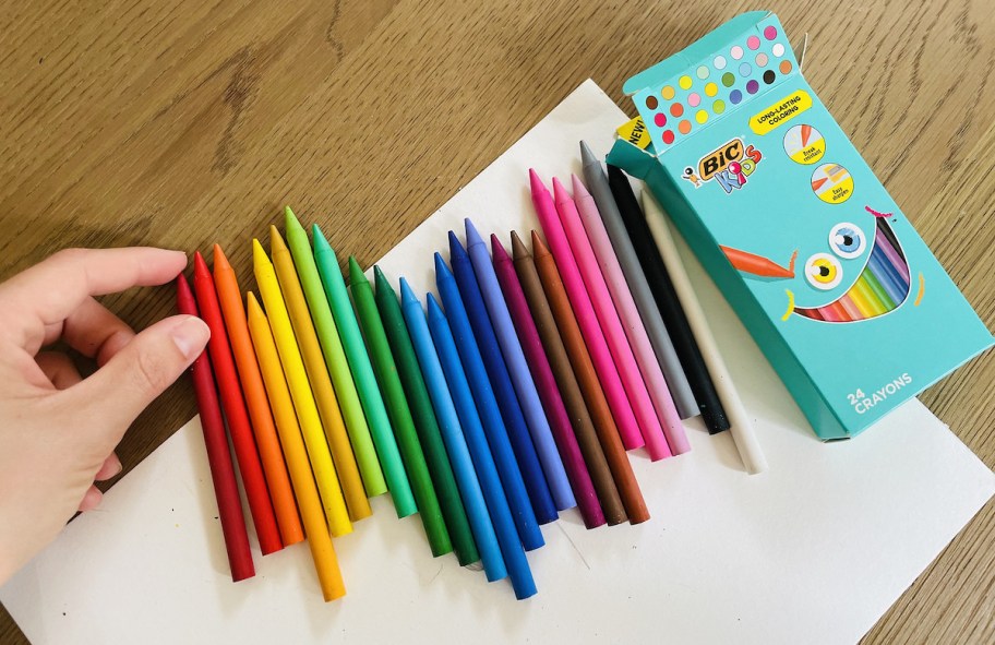 hand holding red crayons from rainbow line of crayons on table