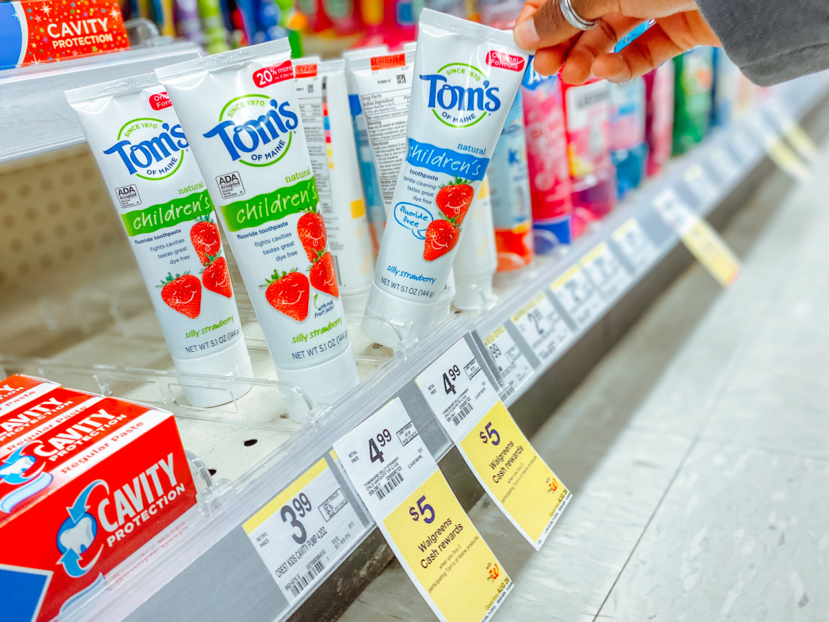 hand tipping a tube of toms of maine kids toothpaste of a ashelf filled with more oral care