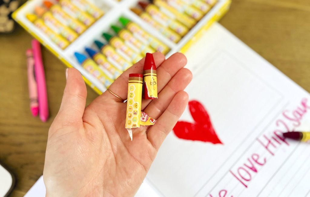 hand holding a brilliant bee red crayons over heart paper