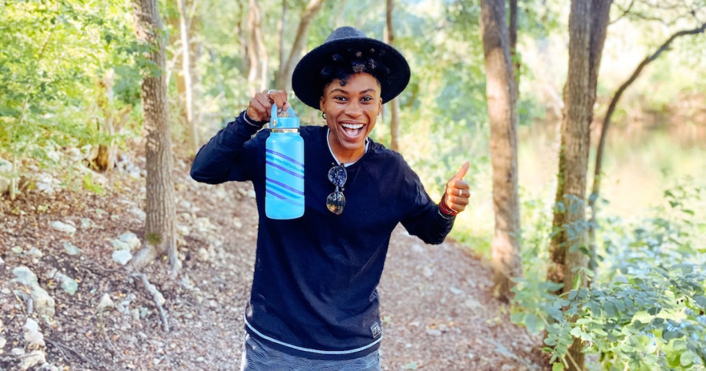 woman standing in forrest holding up hydro flask water bottle