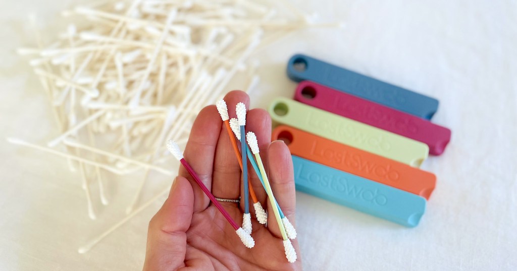 hand holding colorful qtips over pile of white ear swabs