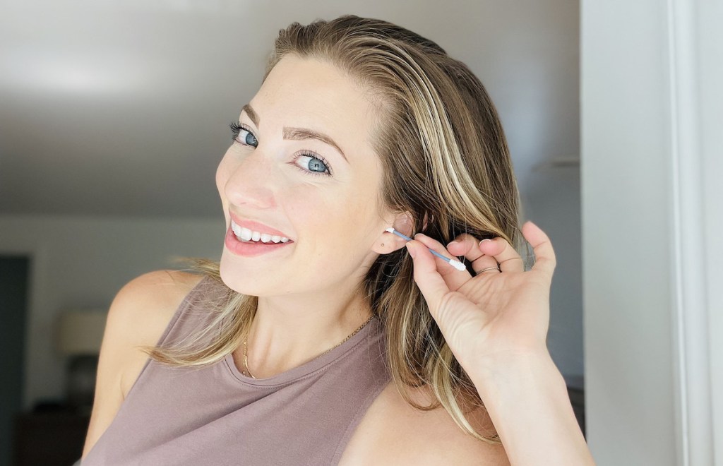 woman putting q-tip in ear smiling at camera