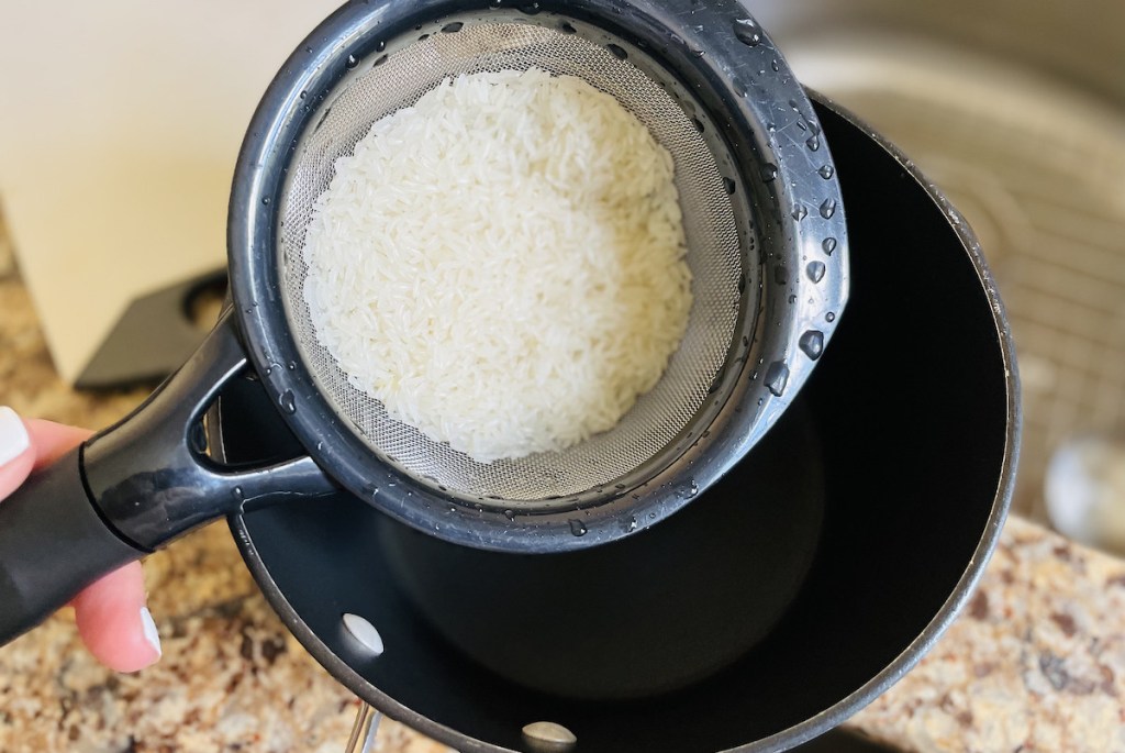 strainer with wet rice inside over empty pot