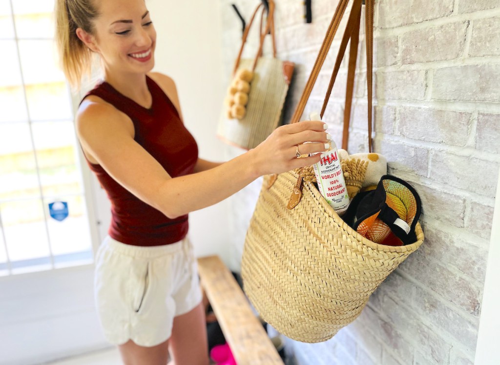 woman putting thai crystal deodorant in beach tote bag hanging on brick wall