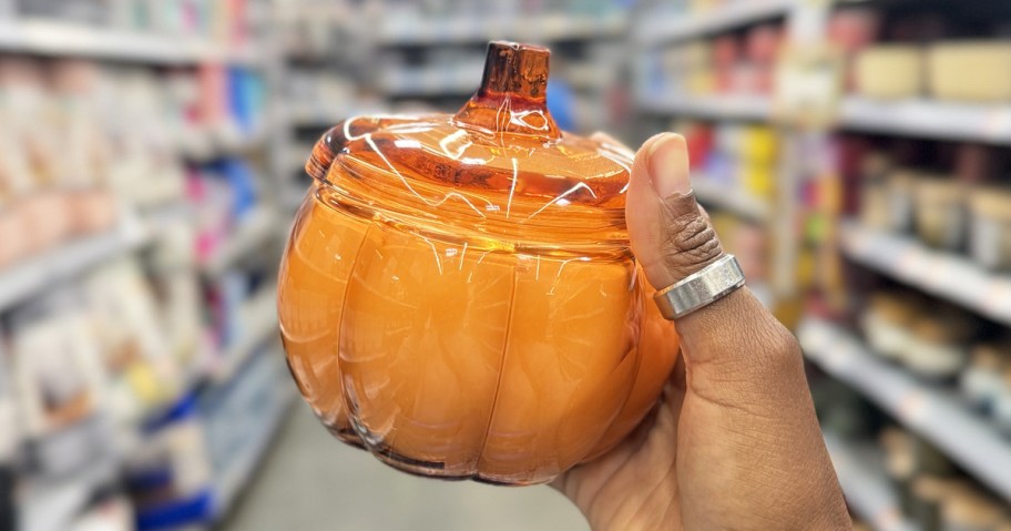 hand holding up an orange pumpkin jar candle