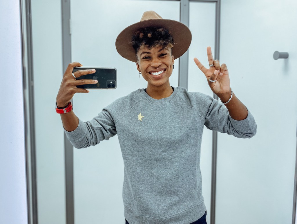 woman giving peace sign taking selfie in mirror with phone