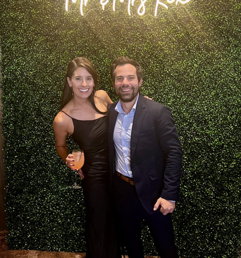 couple standing in front of boxwood wall with lights