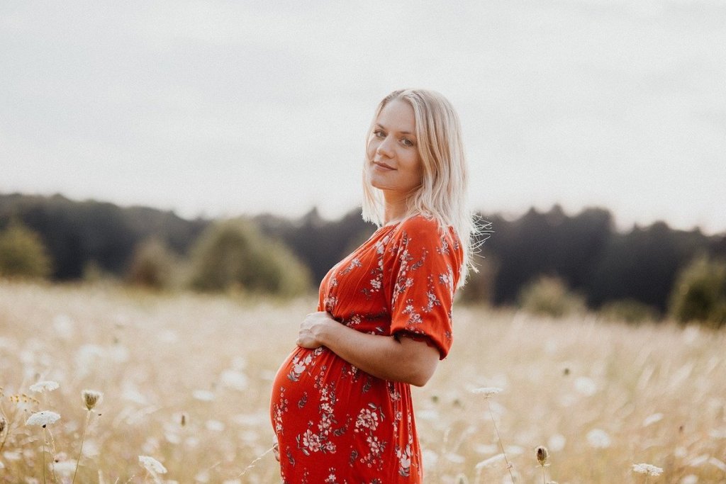 pregnant woman standing outside in field while holding belly