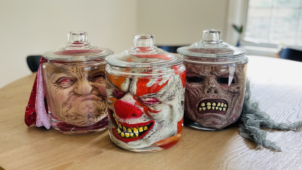 creepy halloween face masks in clear glass jars on wood table