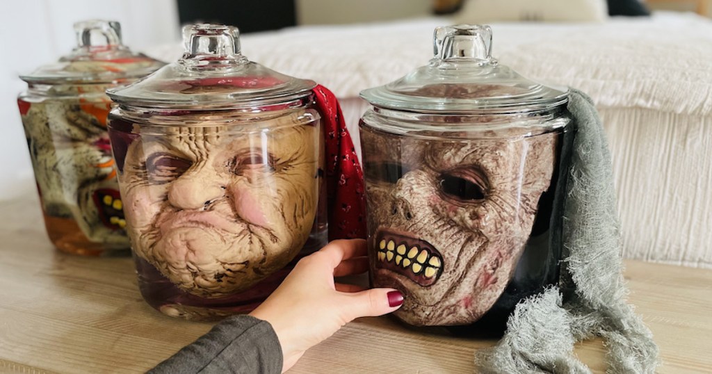 hand holding side of glass jar with creep halloween face masks in jar