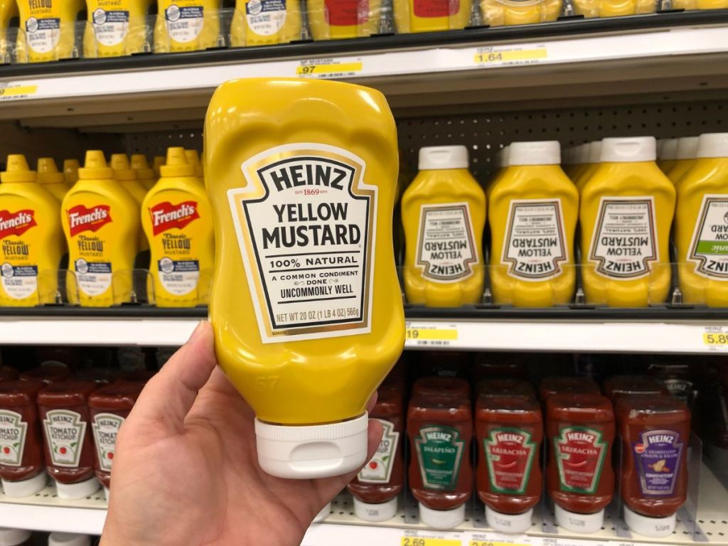 a hand holding a bottle of Heinz yellow mustard in a store