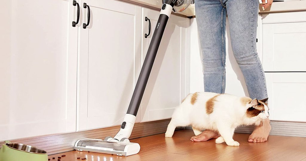 woman using stick vacuum in kitchen