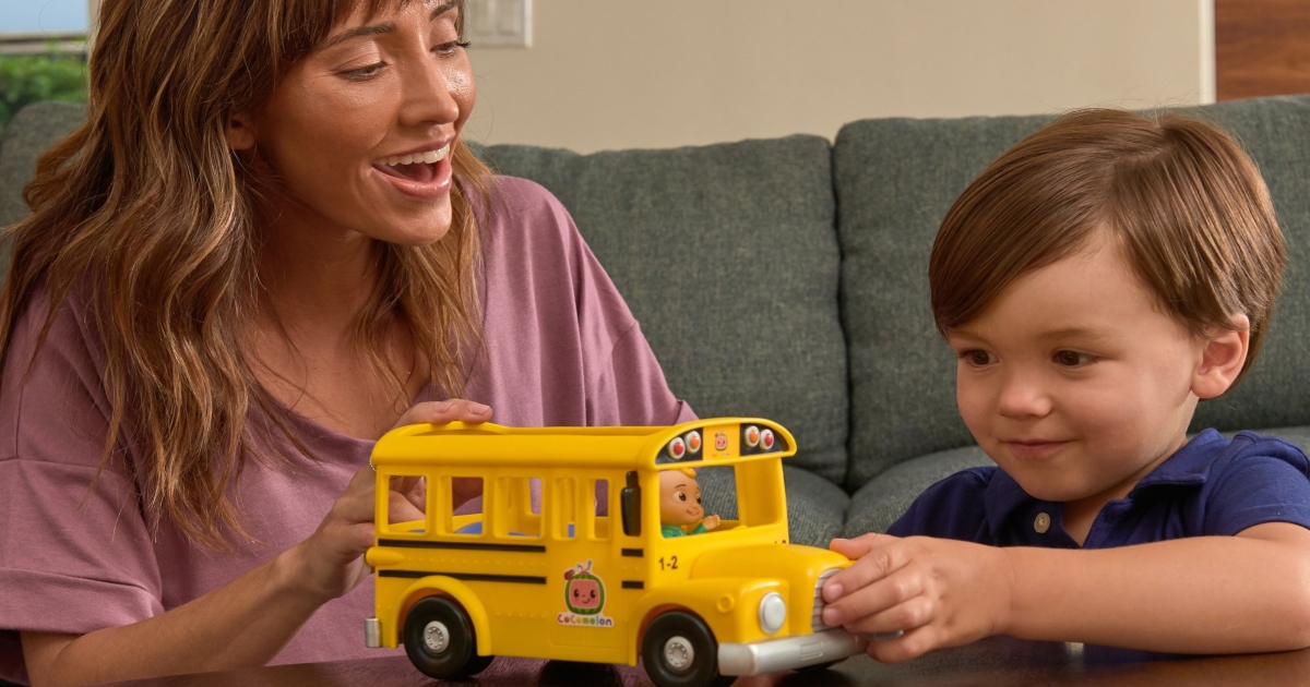 boy playing with Cocomelon school bus on a table with his mom