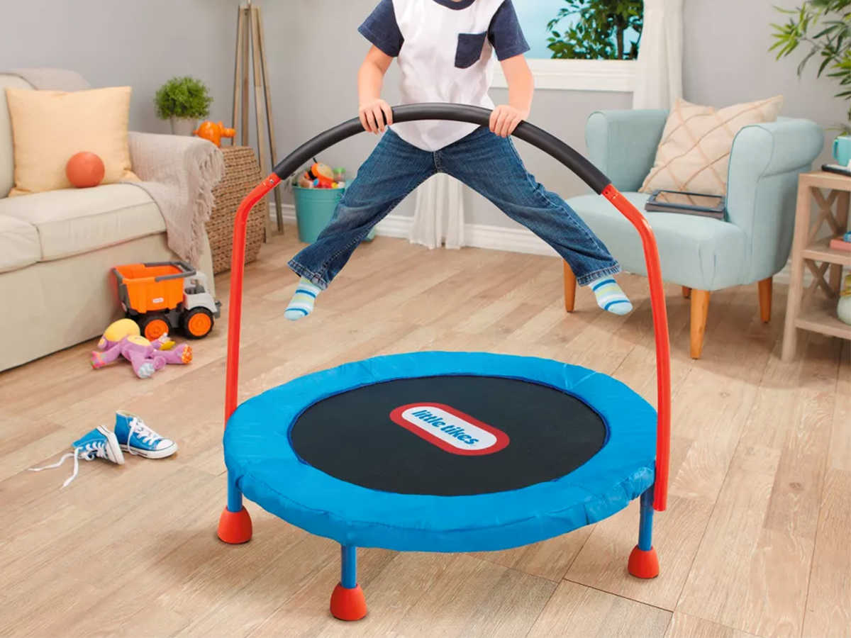 young boy jumping on a little tikes easy store trampoline in a living room with furniture and toys