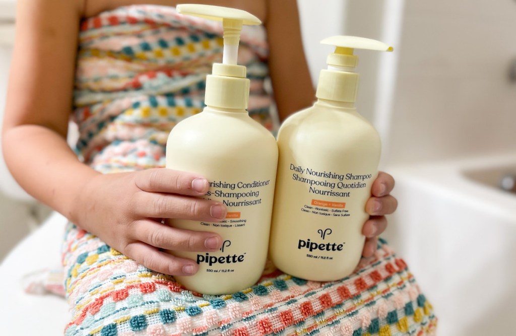 kid wrapped in colorful towel holding pipette shampoo and conditioner