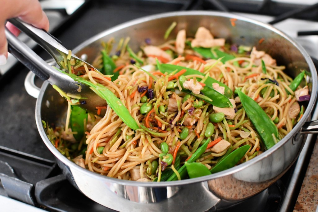 using tongs to mix chow mein