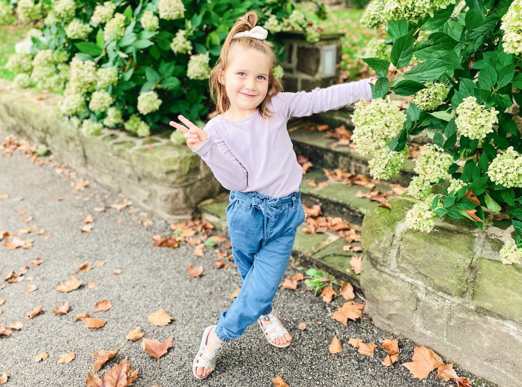 girl giving peace sign standing next to hydrangea plants