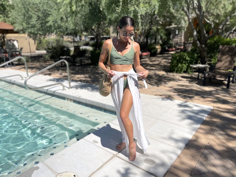 woman standing next to inground pool wearing green bathing suit top and white skirt