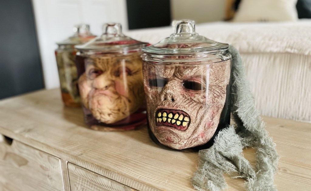 creepy halloween face masks in jars on wood storage bench