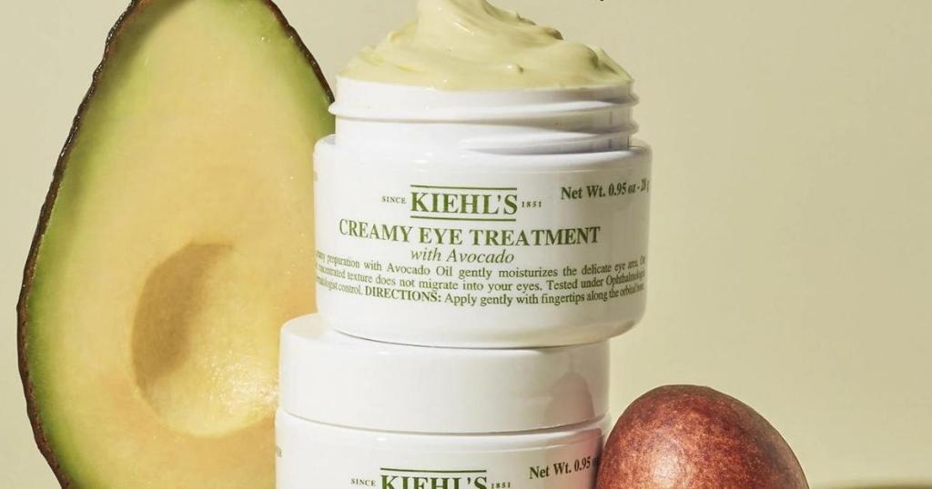 2 jars of Kiehl's Creamy Eye Treatment with Avocado stacked with open avocado behind them and avocado pit beside them