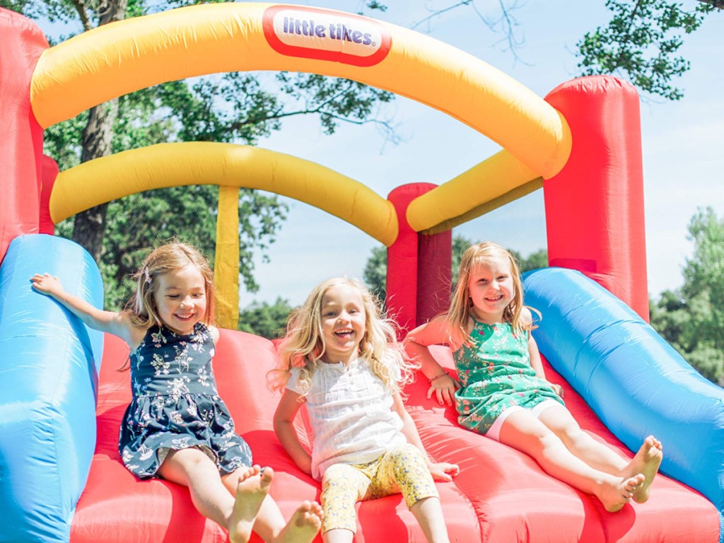 three smiling & laughing young girls sliding down a little tikes bounce house