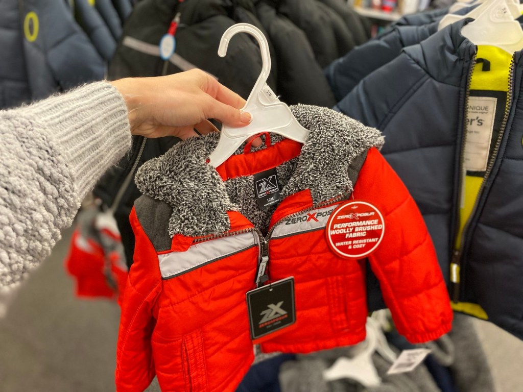 woman holding red kids puffer jacket in store