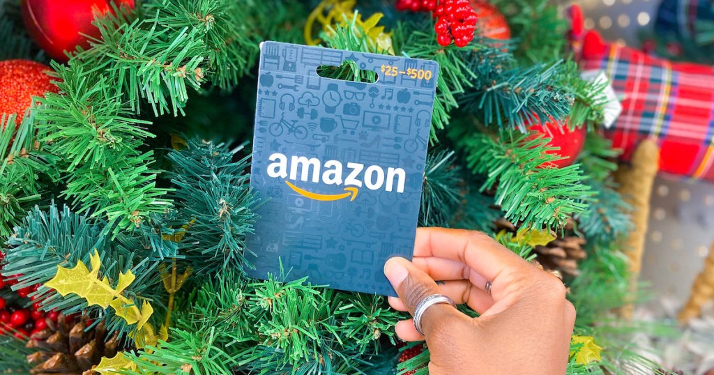 hand holding an amazon gift card in front of christmas garland