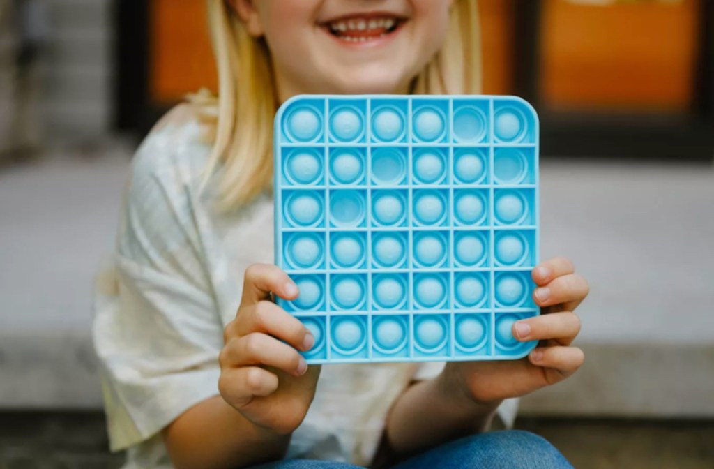 girl holding blue pop it fidget toy - hot toys for christmas