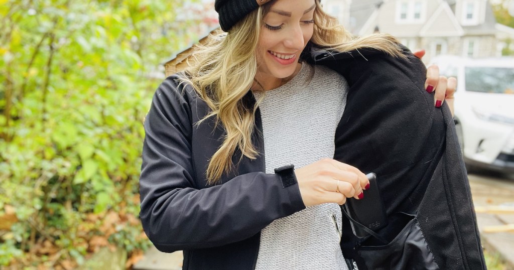 woman putting battery pack into inside of black heated jacket standing outside - gift ideas people who are always cold